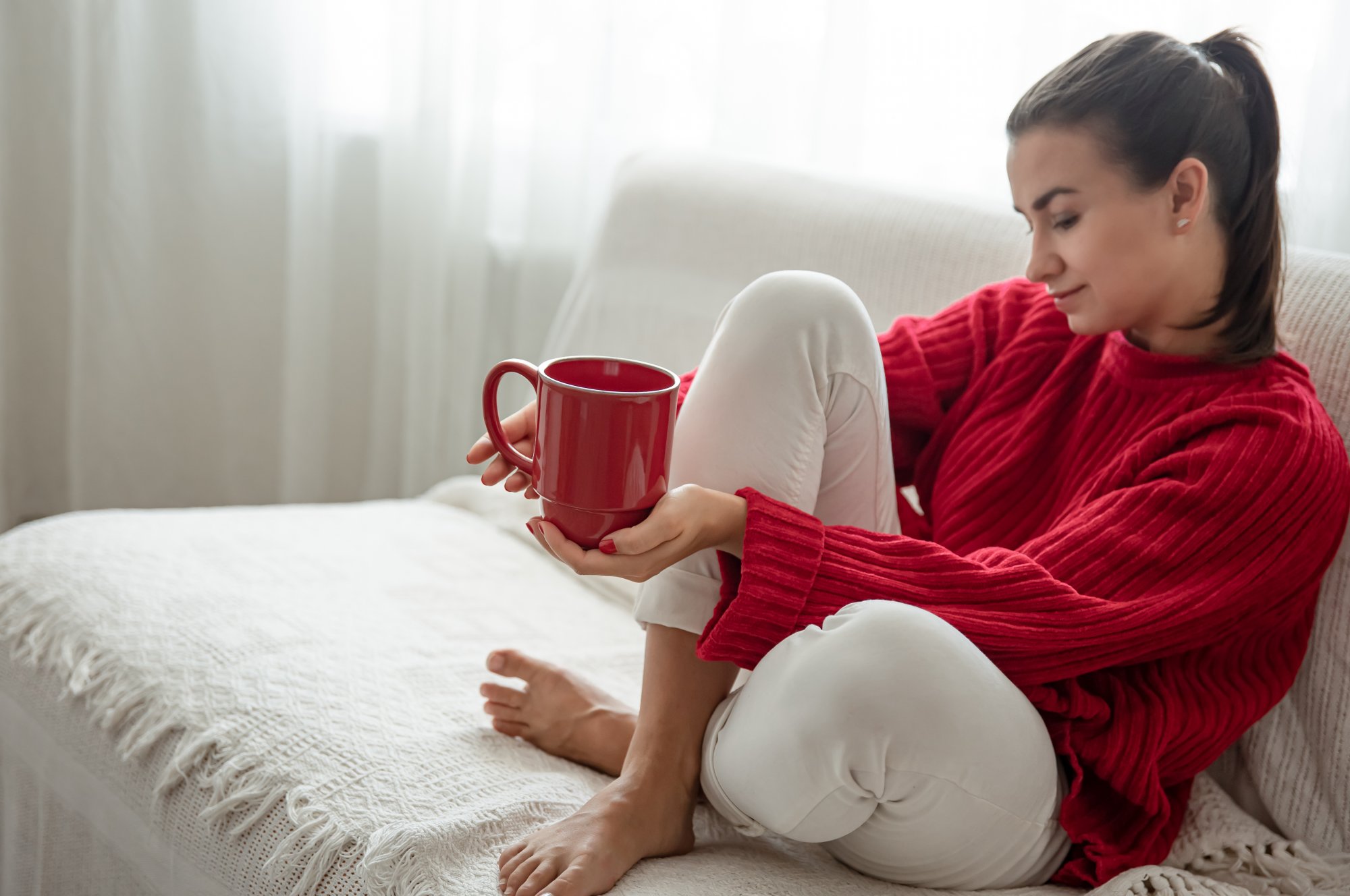 young-woman-with-red-cup-hot-drink-cozy-red-sweater-is-resting-couch-home-copy-space.jpg